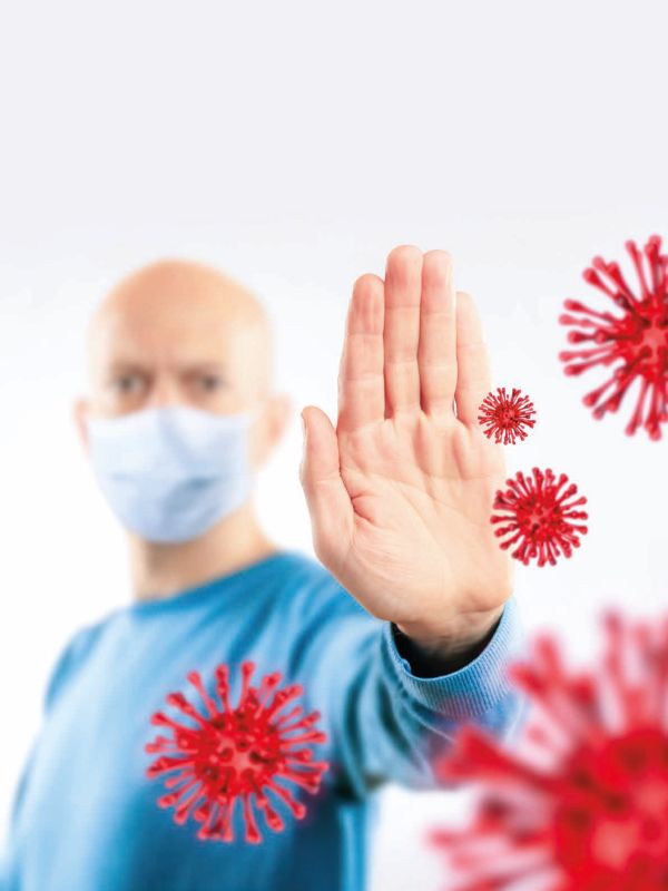 Covid-19 und Influenza – 6 Gründe, warum Coronavirus und Grippevirus nicht vergleichbar sind: Das Bild zeigt links im Hintergrund schemenhaft einen Mann mit Mund-Nasen-Bedeckung, der seinen linken Arm ausgestreckt hat, um mit seiner linken mittig im Vordergrund zu sehenden Hand rot gezeichnete, stark vergrößerte Viren zu stoppen.