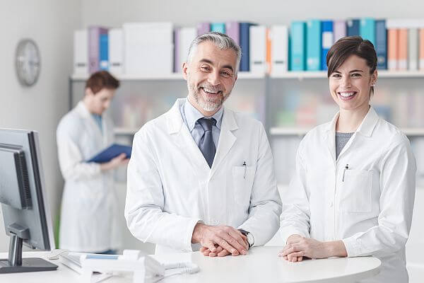 Ein Arzt und eine Ärztin im weißen Kittel lächeln in Kamera
