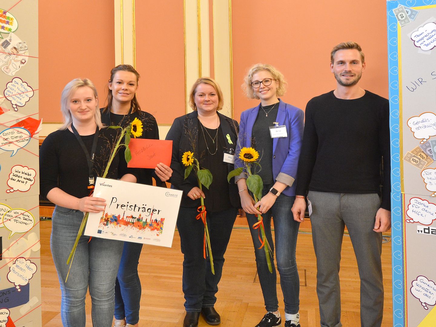Engagement in der Pflege im Krankenhaus in Berlin-Schöneberg: Fünf Mitarbeitende, die eine Auszeichnung und Sonnenblumen erhalten haben, lächeln in Richtung Kamera.