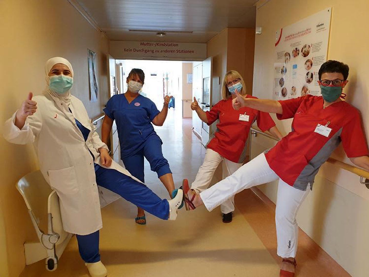 2 Pflegekräfte, 1 Hebamme & 1 Ärztin der Geburtsmedizin begrüßen sich per "Fußschlag" im Klinikgang am Humboldt-Klinikum