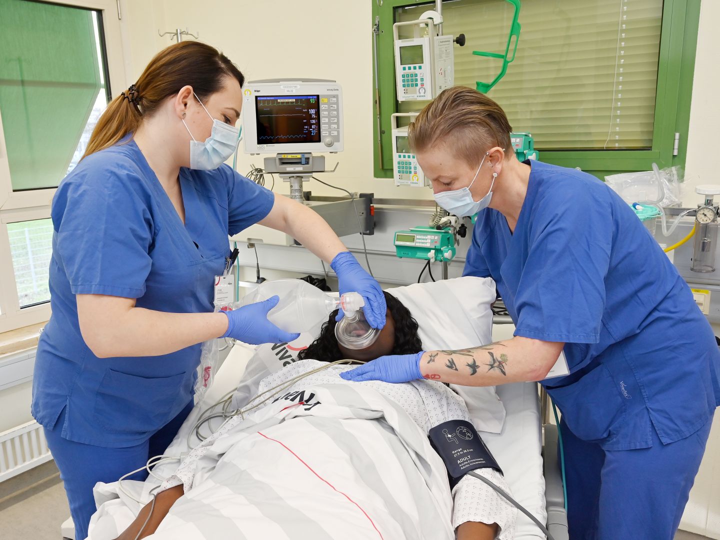Pflege im Krankenhaus in Berlin-Kreuzberg: Zwei weibliche Pflegekräfte stehen an einer OP-Liege, in der eine Patientin liegt. Die Pflegerin links beatmet die Patientin mithilfe eines Beatmungsbeutels.