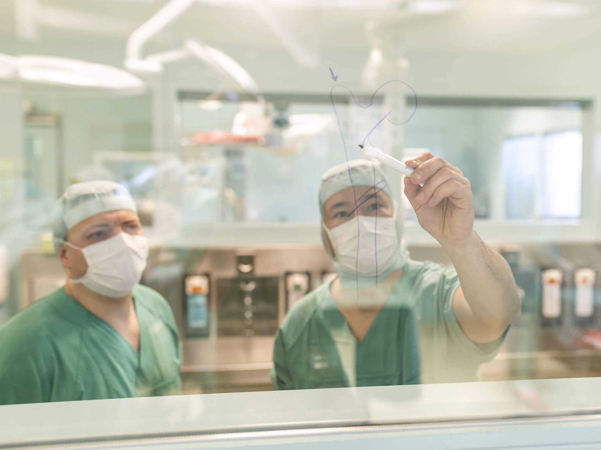 Chefarzt zeichnet einen Oberschenkelknochen auf die Glaswand im OP
