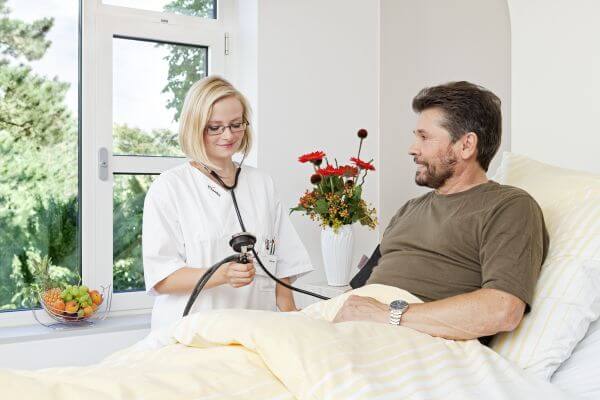 Pflegerin misst Blutdruck bei Patient im Bett