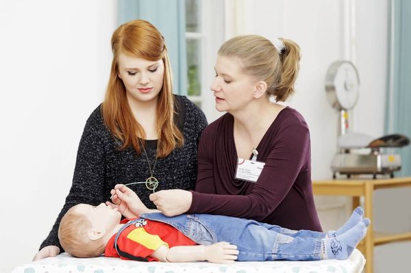 Praxisanleiterin zeigt Pflegeschülerin die Intubation eines Kleinkindes