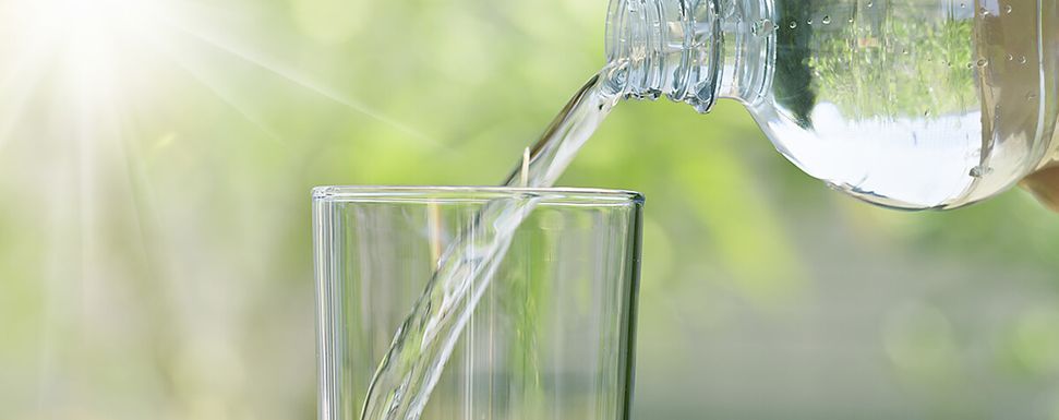 Ein Glas wird mit Wasser aus einer Flasche gefüllt
