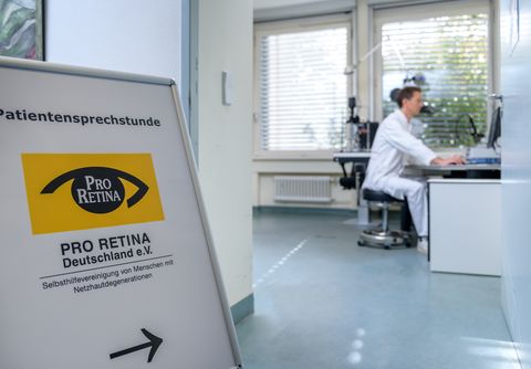 Schild mit "Pro Retina" zeigt in ein Büro, wo ein Arzt am Computer sitzt