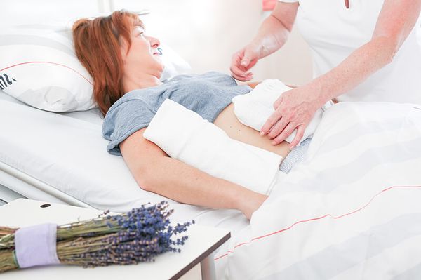 Patientin liegt auf einem Bett in der Krebstherapie, auf dem Patiententisch sieht man einen Lavendelstrauß