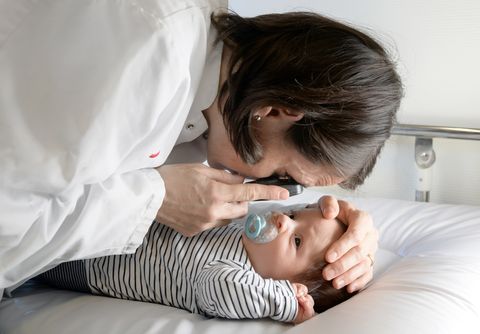 Ärztin beugt sich über Neugeborenes und untersucht mit Lupe das Auge