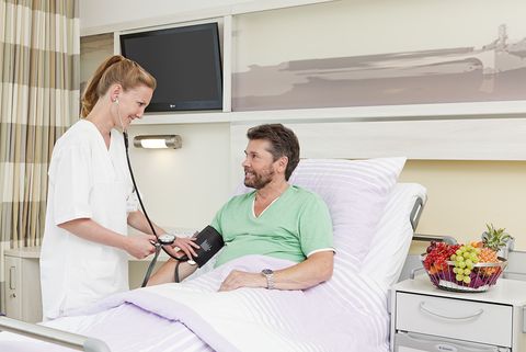 Pflege im Krankenhaus Neukölln: Das Bild zeigt eine Pflegerin, die den Blutdruck einen im Bett liegenden Patienten misst.