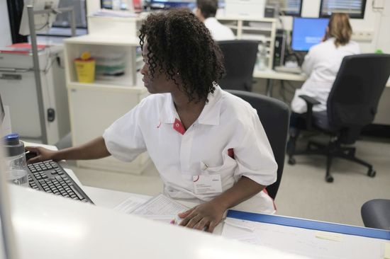 Pflegejobs im Krankenhaus Neukölln: Eine weibliche Pflegefachkraft sitzt am Schreibtisch.